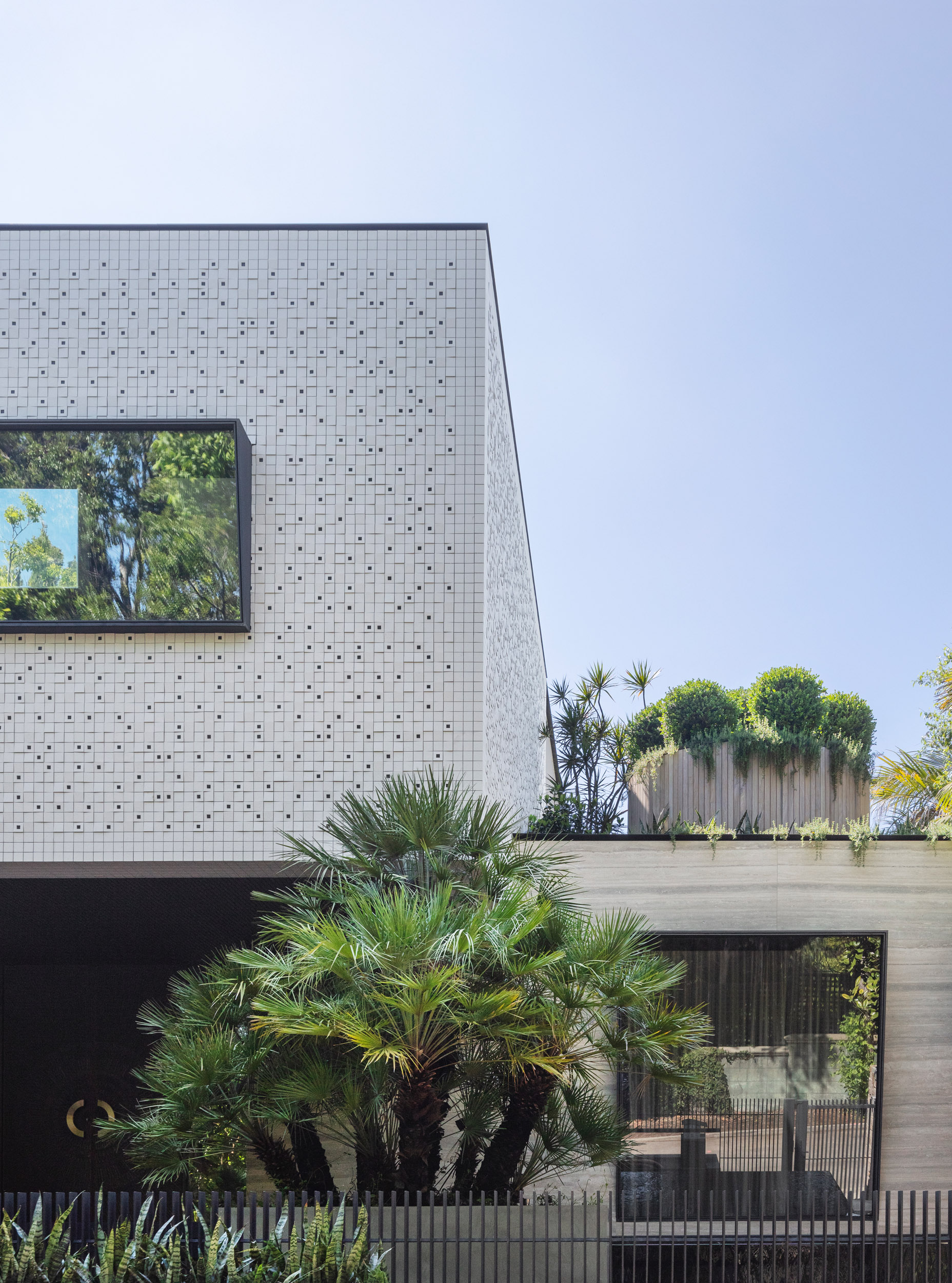 European fan palms offset clean architectural lines at Sydney property. Soft landscaping complements the built-structure, a contemporary home clad in Inax mosaic tiles, travertine and glass.