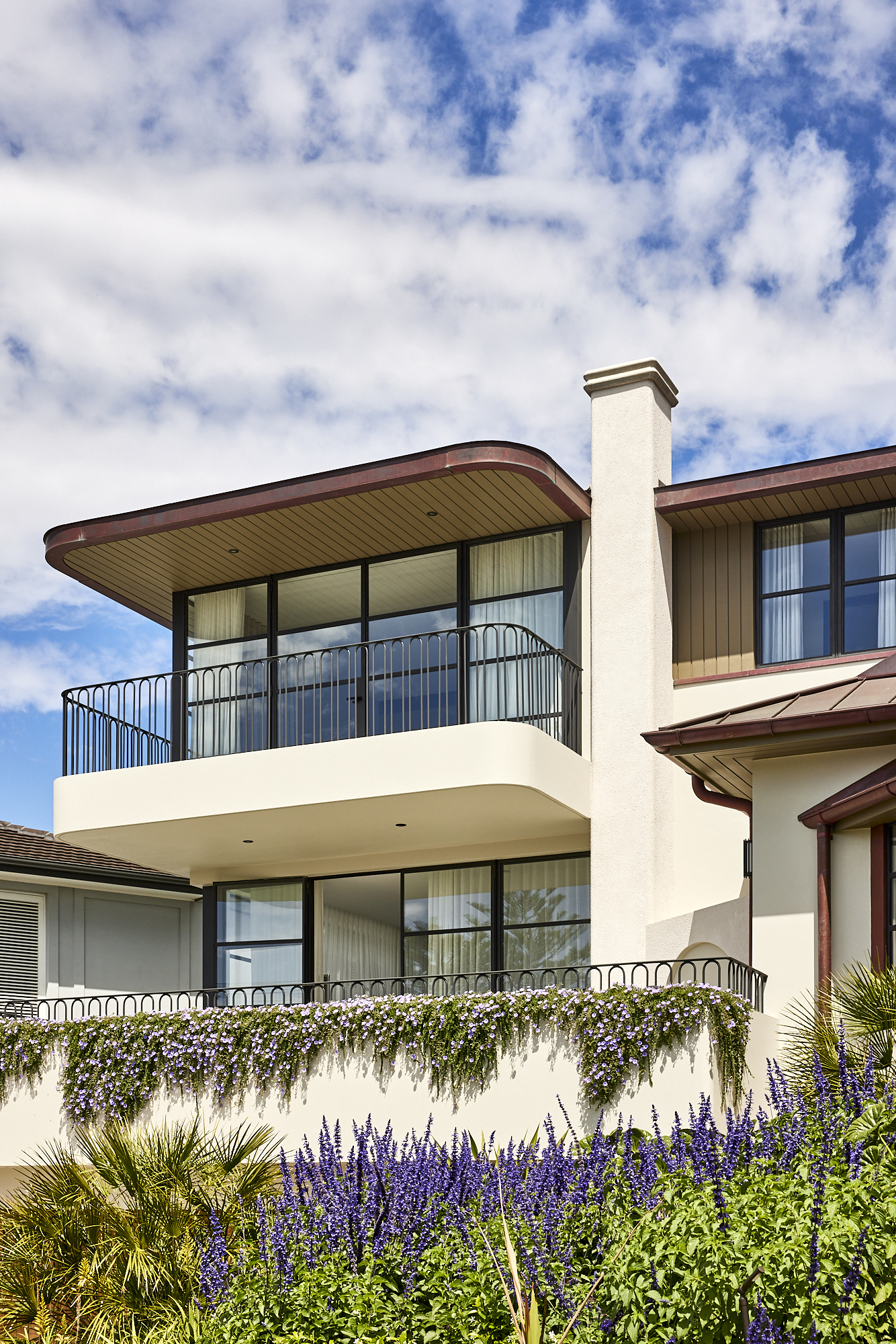 Modern architectural home with curved detail landscape design features spilling garden beds and purple plants